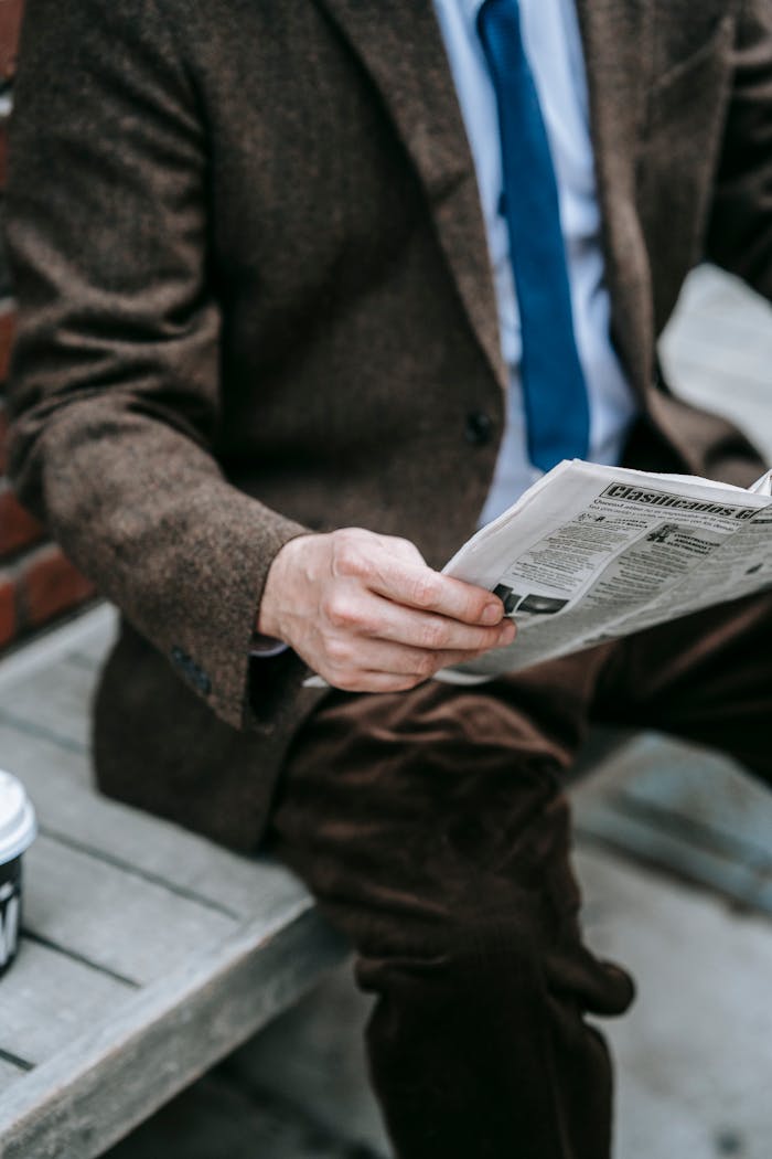 who-we-are Business professional in brown suit reading newspaper outdoors. Urban style, winter fashion.